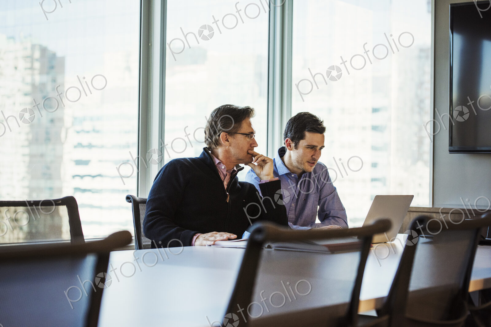 Two men at a table in a meeting room looking at a laptop computer.
