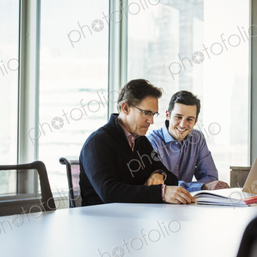 Two men at a table in a meeting room looking at a laptop computer.