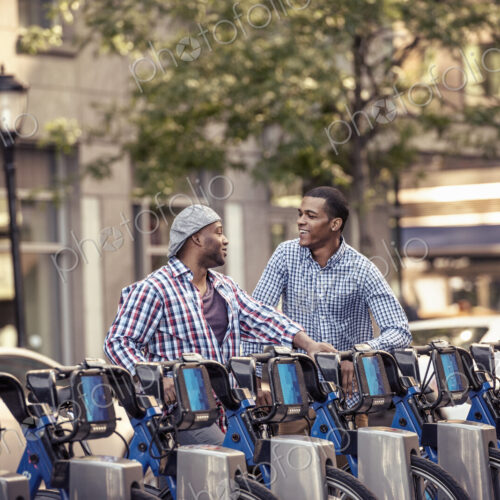 Two men by a rack of bicycles for hire in a city park