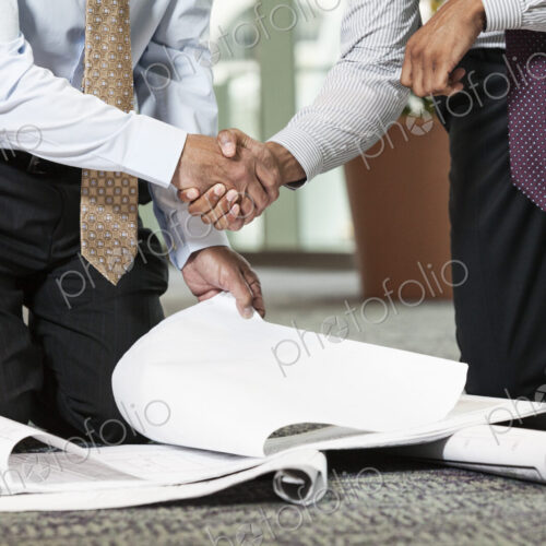 Two men going over plans for a new office space while kneeling on an office carpet. Two men going over plans for a new office space while kneeling on an office carpet.