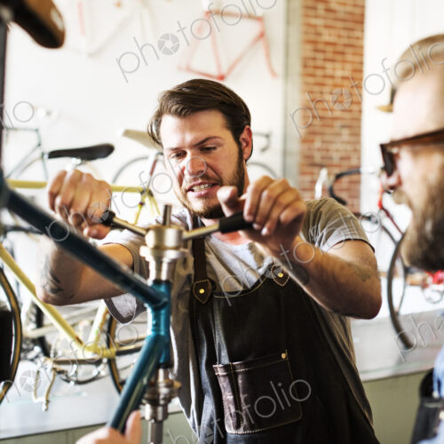 Two men in a cycle repair shop, looking at a bicycle. Two men in a cycle repair shop, looking at a bicycle.