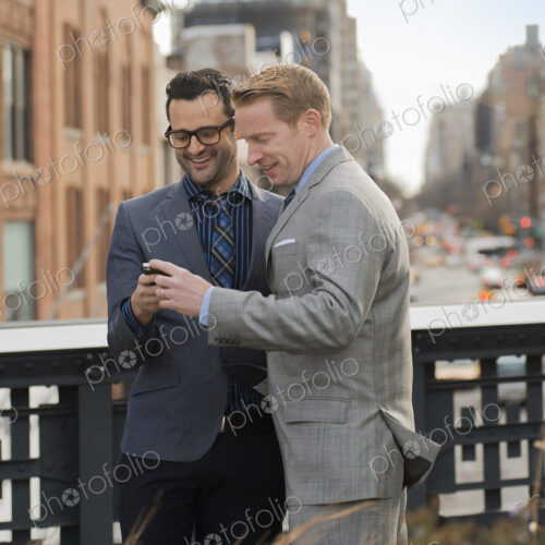 Two men in formal business clothes, standing side by side, looking at a cell phone… Two men in formal business clothes, standing side by side, looking at a cell phone…