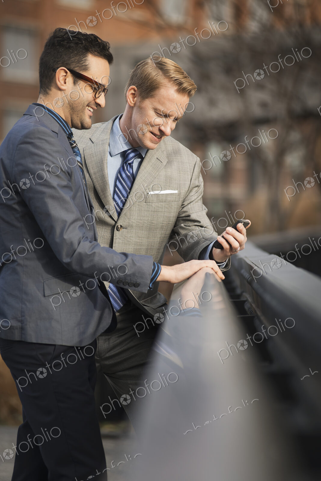 Two men in formal business clothes, standing side by side, looking at a cell phone…