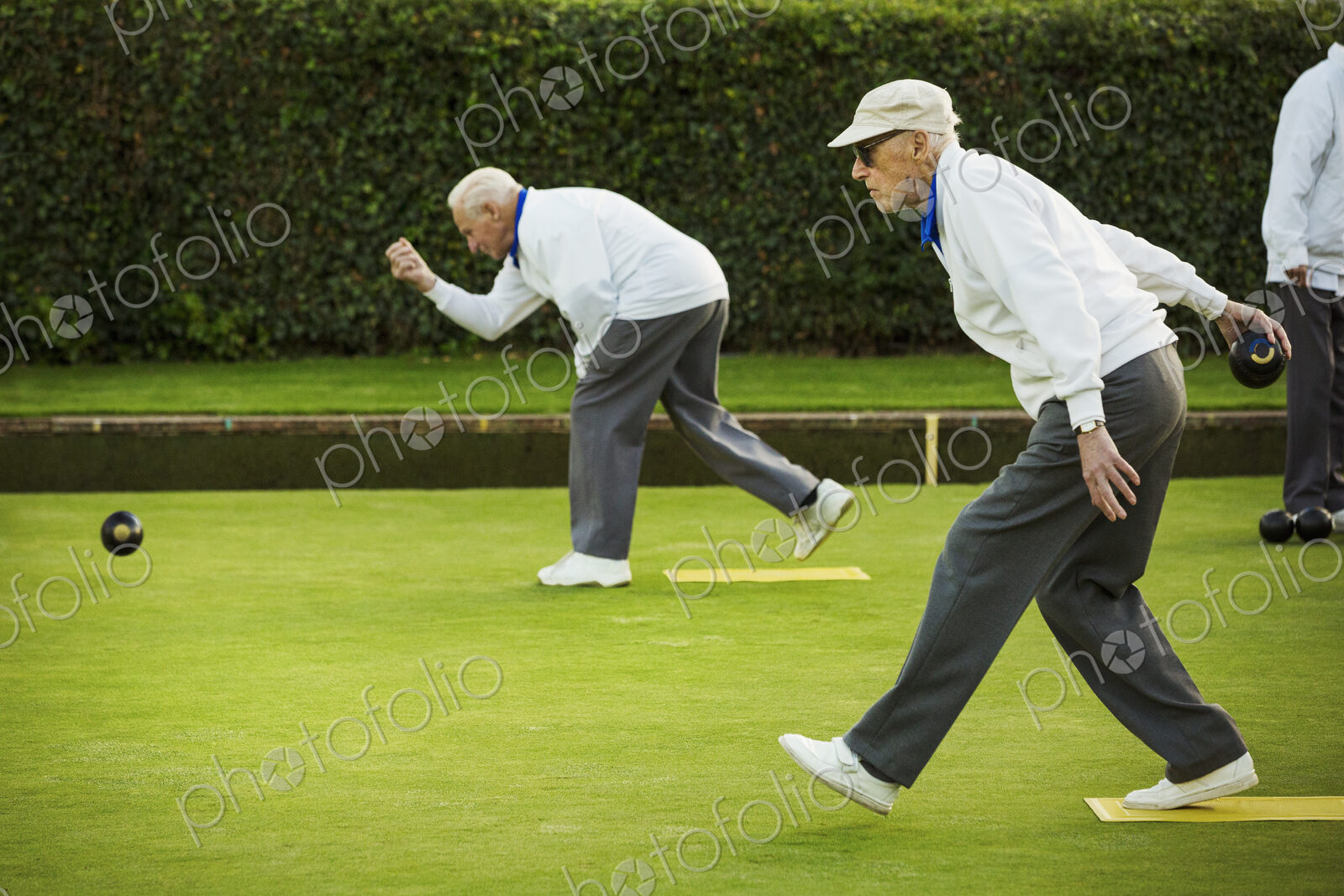 Two men preparing to deliver a lawn bowl shot, bending down and swinging their arms.