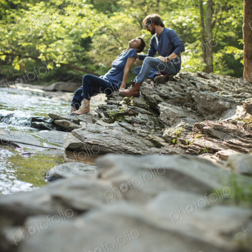 Two men seated in shade on the rocks by the river.