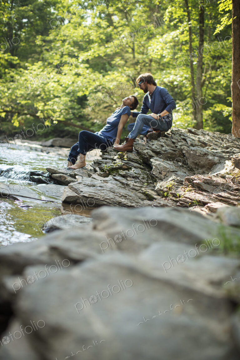 Two men seated in shade on the rocks by the river.