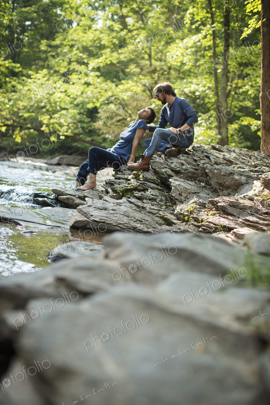 Two men seated in shade on the rocks by the river.