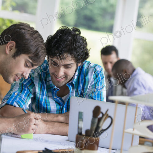 Two men seated, one drawing on paper. Two men seated, one drawing on paper.