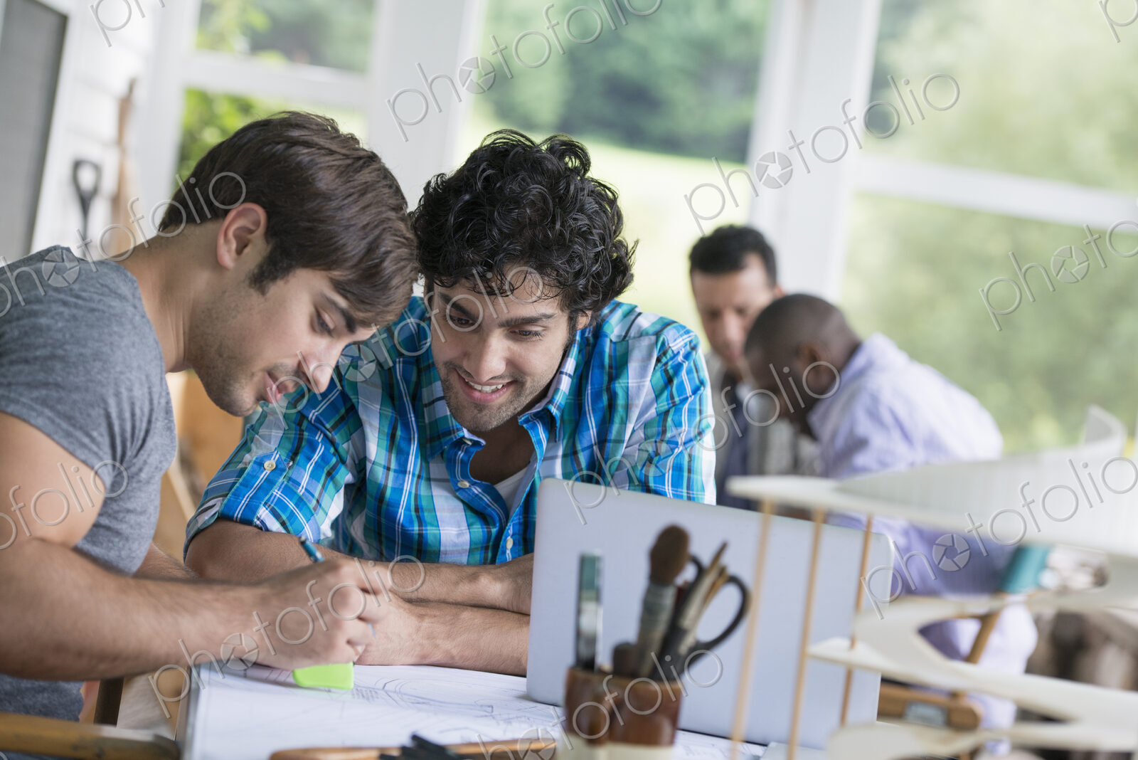 Two men seated, one drawing on paper.