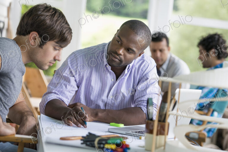 Two men seated, one drawing on paper