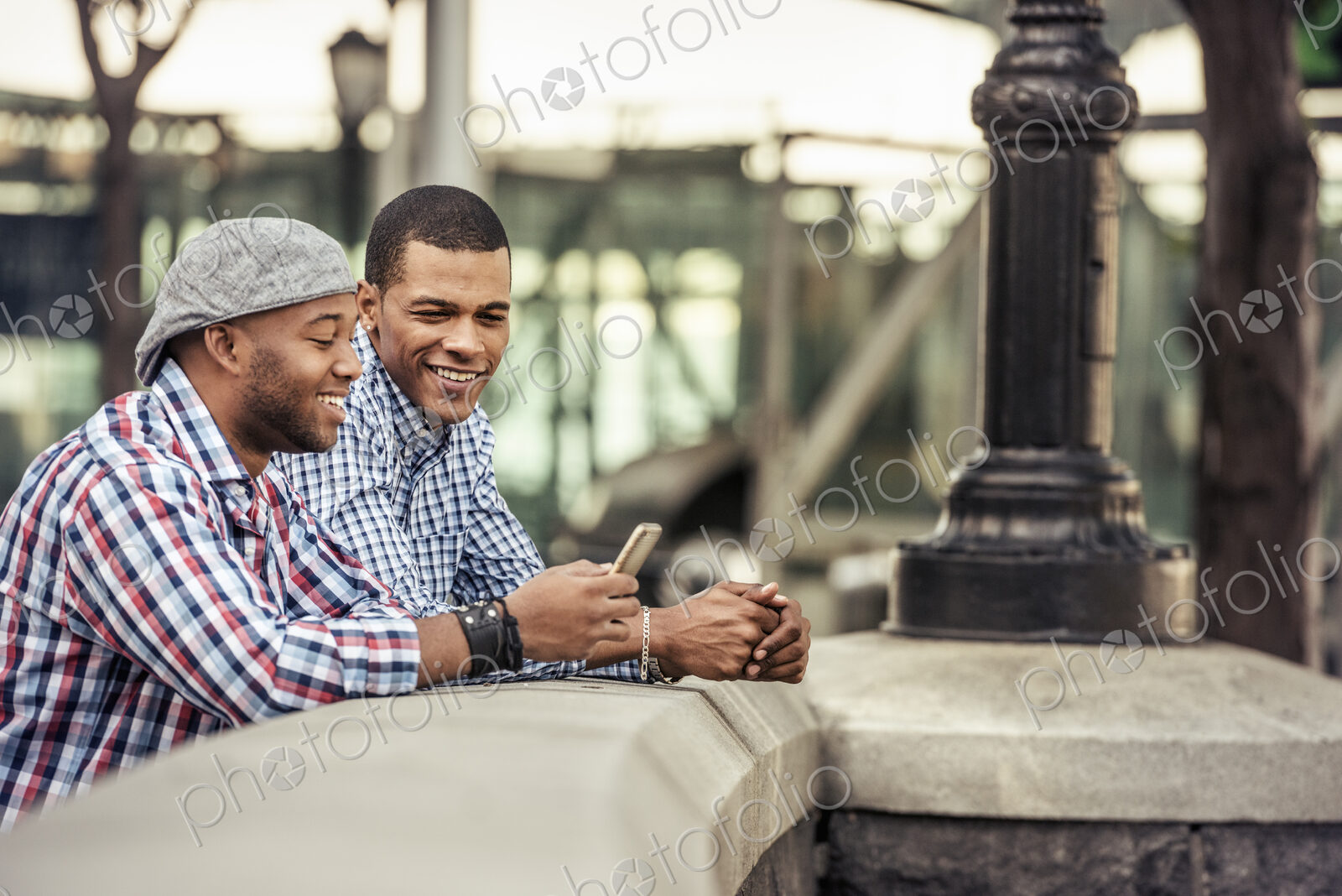 Two men side by side leaning on a parapet by a bridge looking at a smart phone