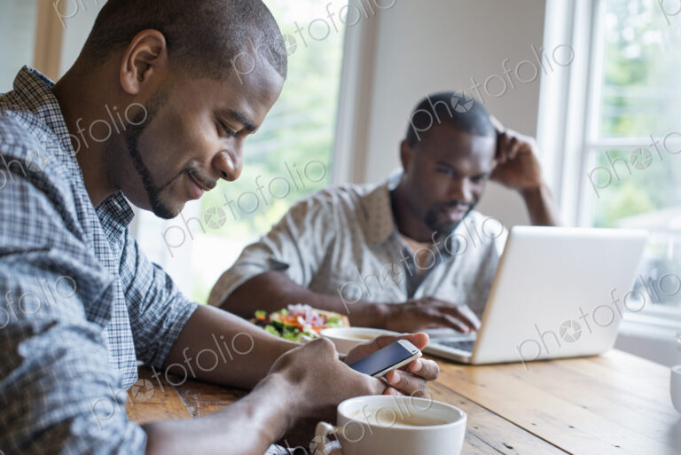 Two men sitting in a cafe. Using a laptop and a smart phone.