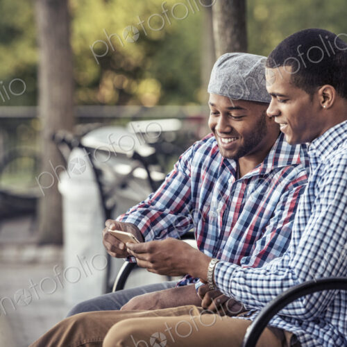 Two men sitting in a park, looking at a smart phone Two men sitting in a park, looking at a smart phone