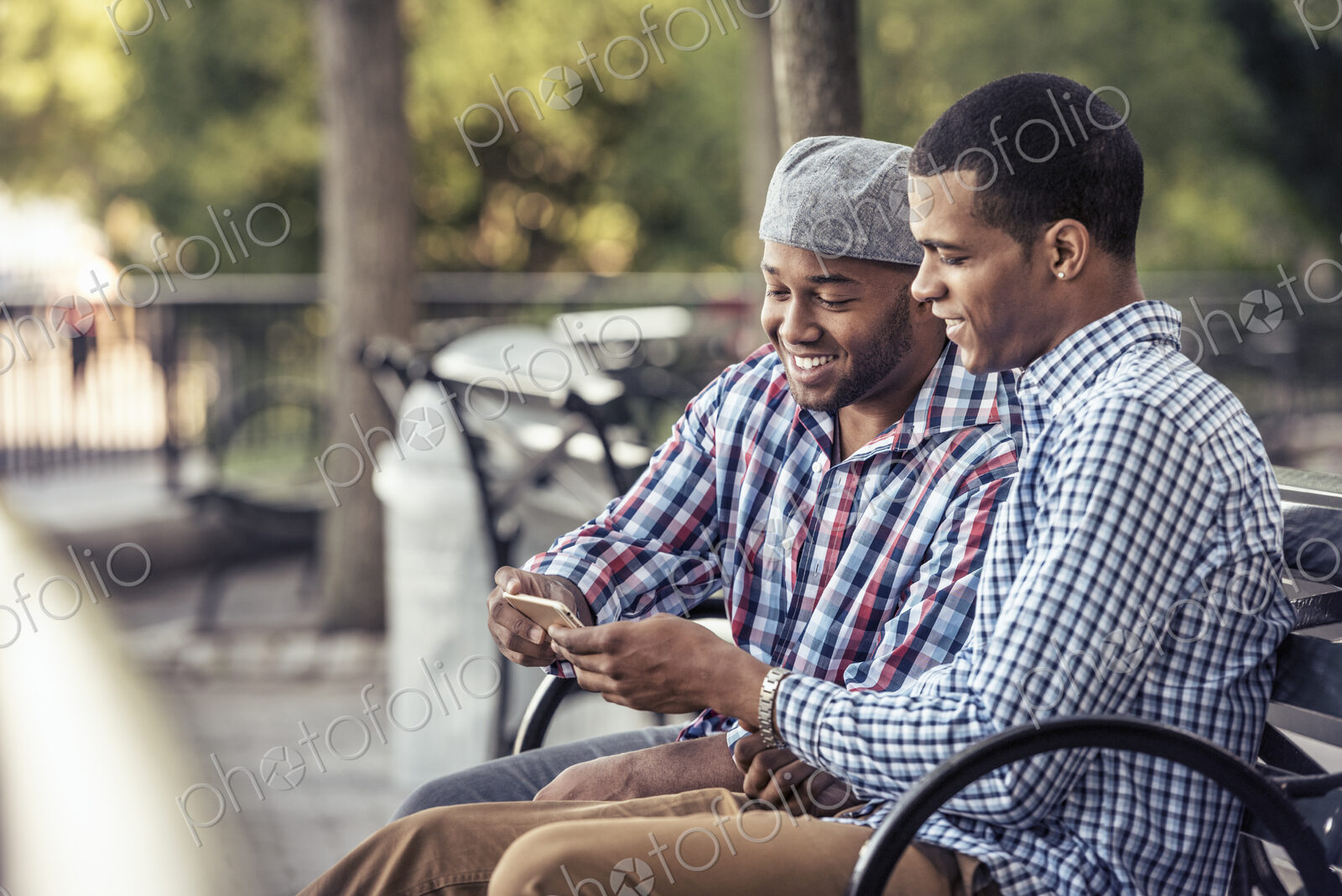 Two men sitting in a park, looking at a smart phone