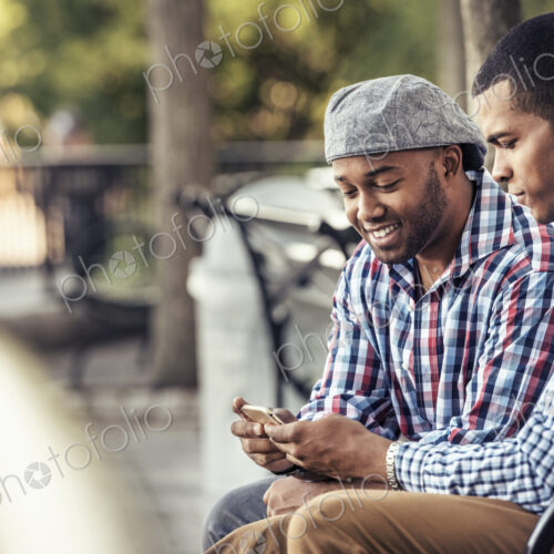 Two men sitting in a park, looking at a smart phone Two men sitting in a park, looking at a smart phone