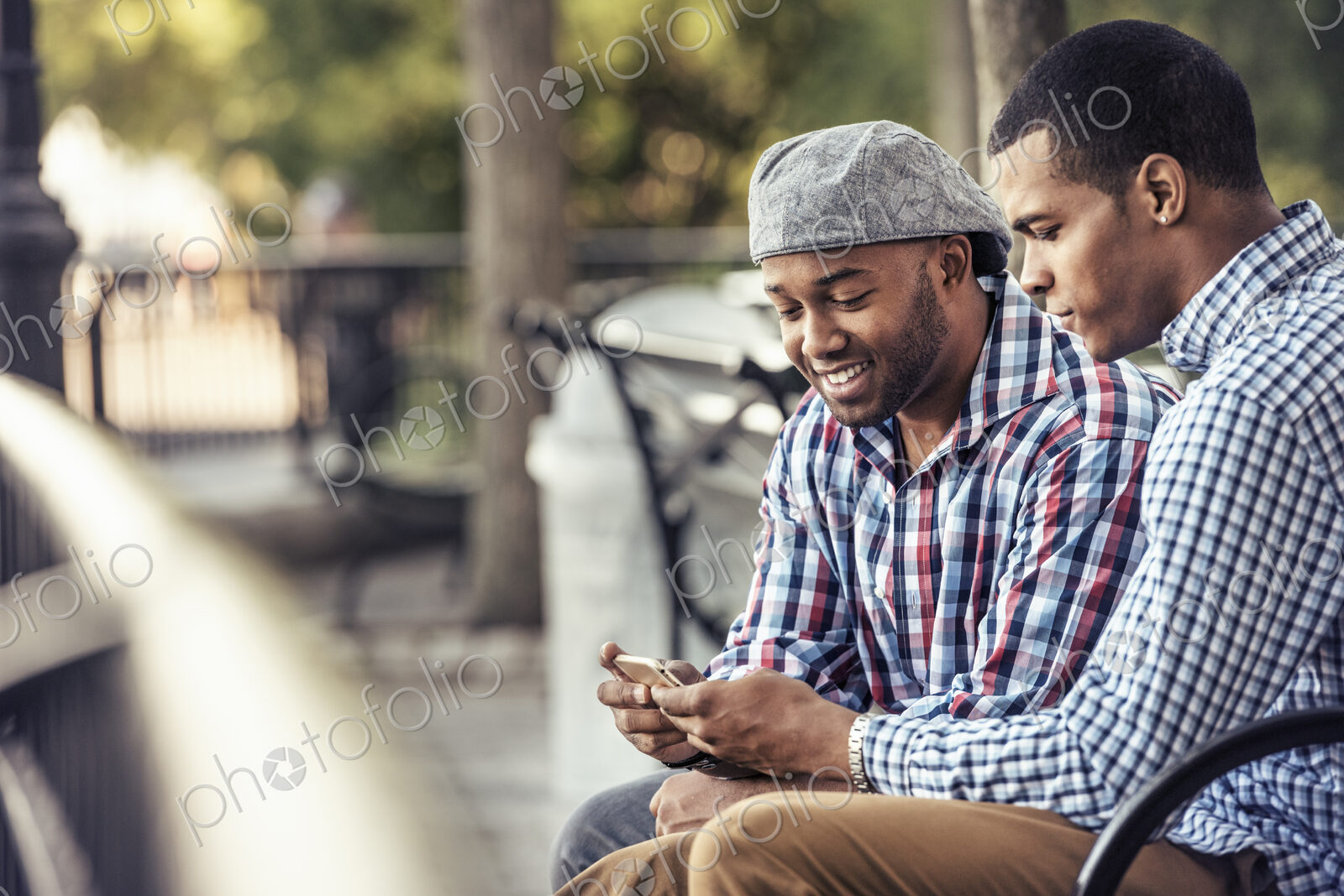 Two men sitting in a park, looking at a smart phone