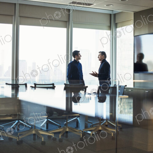 Two men standing at a table in a meeting room talking to each other. Two men standing at a table in a meeting room talking to each other.