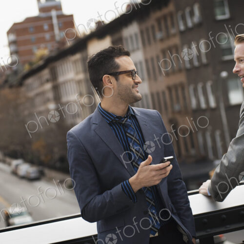 Two men standing talking on an elevated walkway above a city road. Two men standing talking on an elevated walkway above a city road.