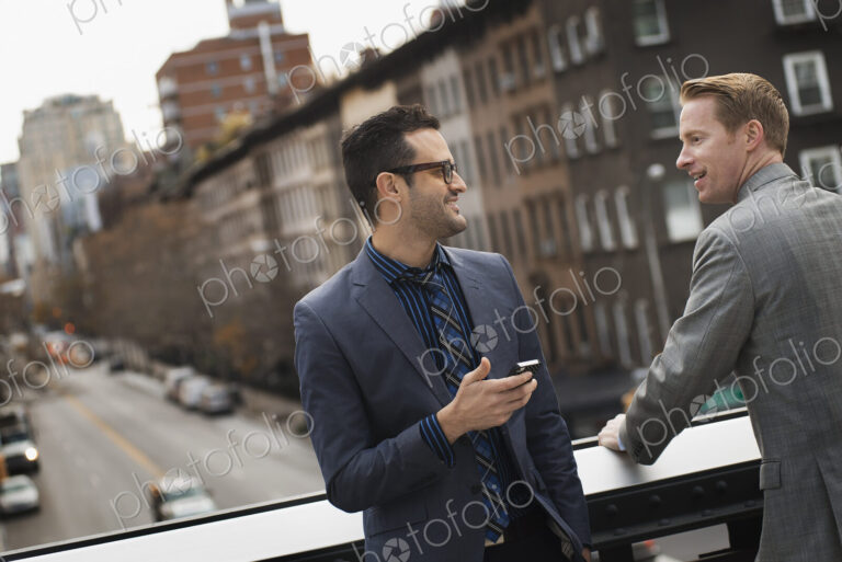 Two men standing talking on an elevated walkway above a city road.