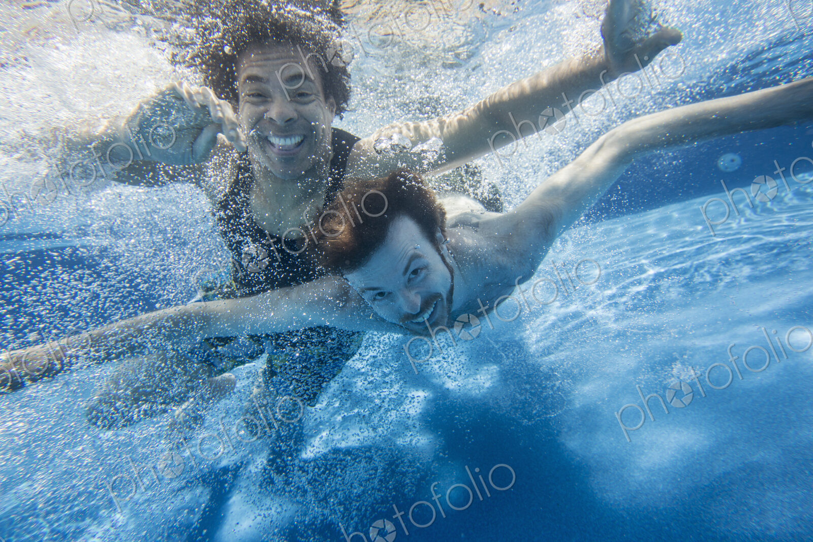 Two men swimming under water in a swimming pool.