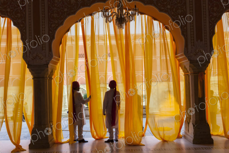 Two men under arch decorated with translucent orange curtains.