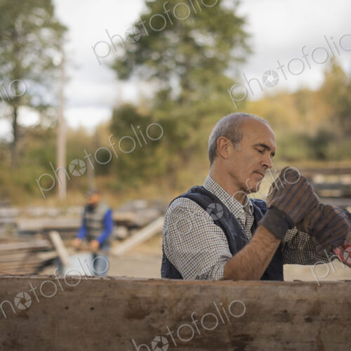 Two men working in a reclaimed timber yard. One using a tool to remove metals from a… Two men working in a reclaimed timber yard. One using a tool to remove metals from a…