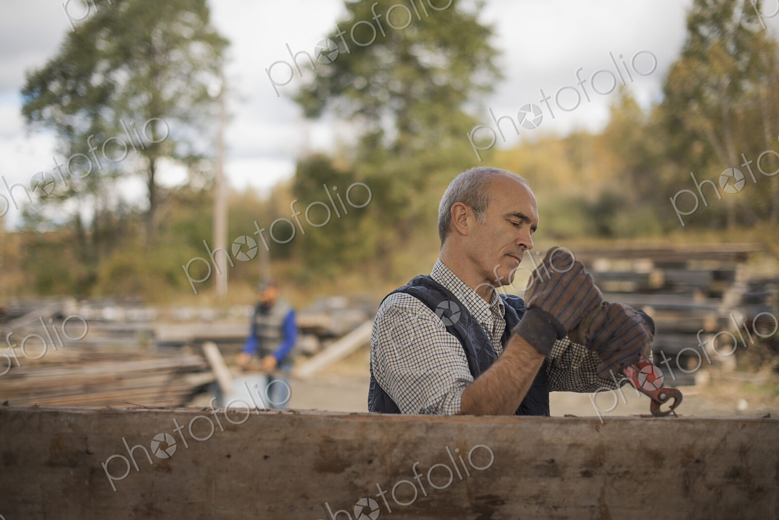 Two men working in a reclaimed timber yard. One using a tool to remove metals from a…