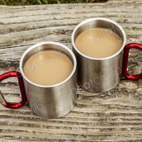 Two metal camping mugs of tea on a wooden table.