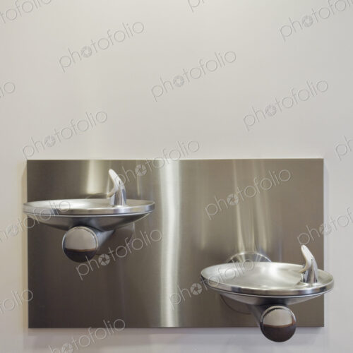 Two metal drinking fountains mounted on wall at different heights.