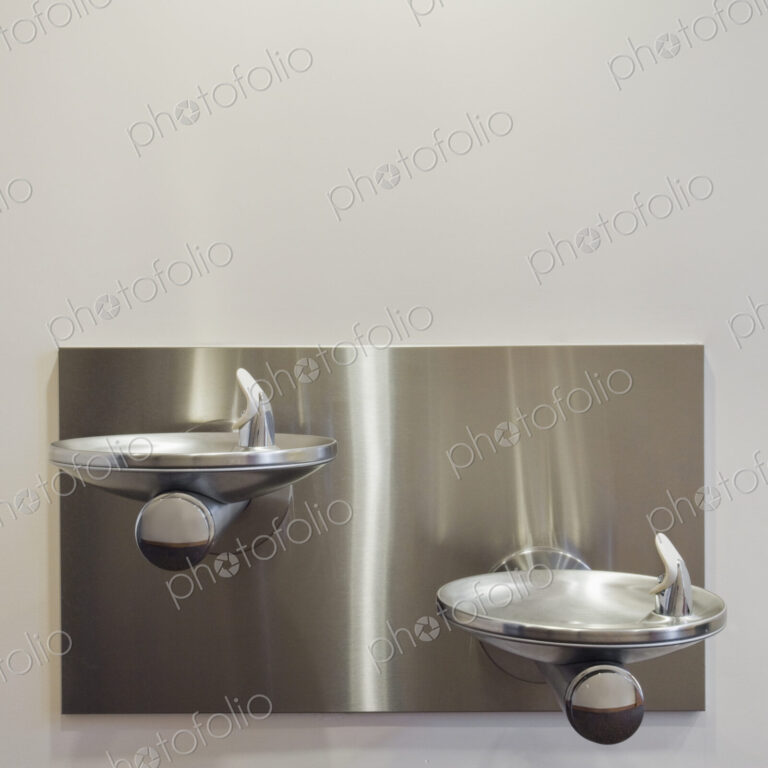 Two metal drinking fountains mounted on wall at different heights.