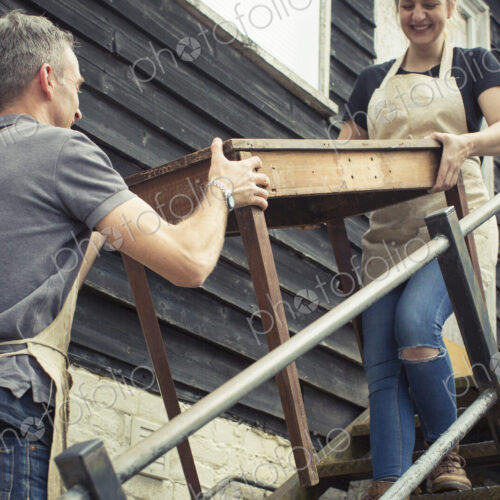 Two people, a man and a young woman carrying an antique wooden table up steps. Two people, a man and a young woman carrying an antique wooden table up steps.