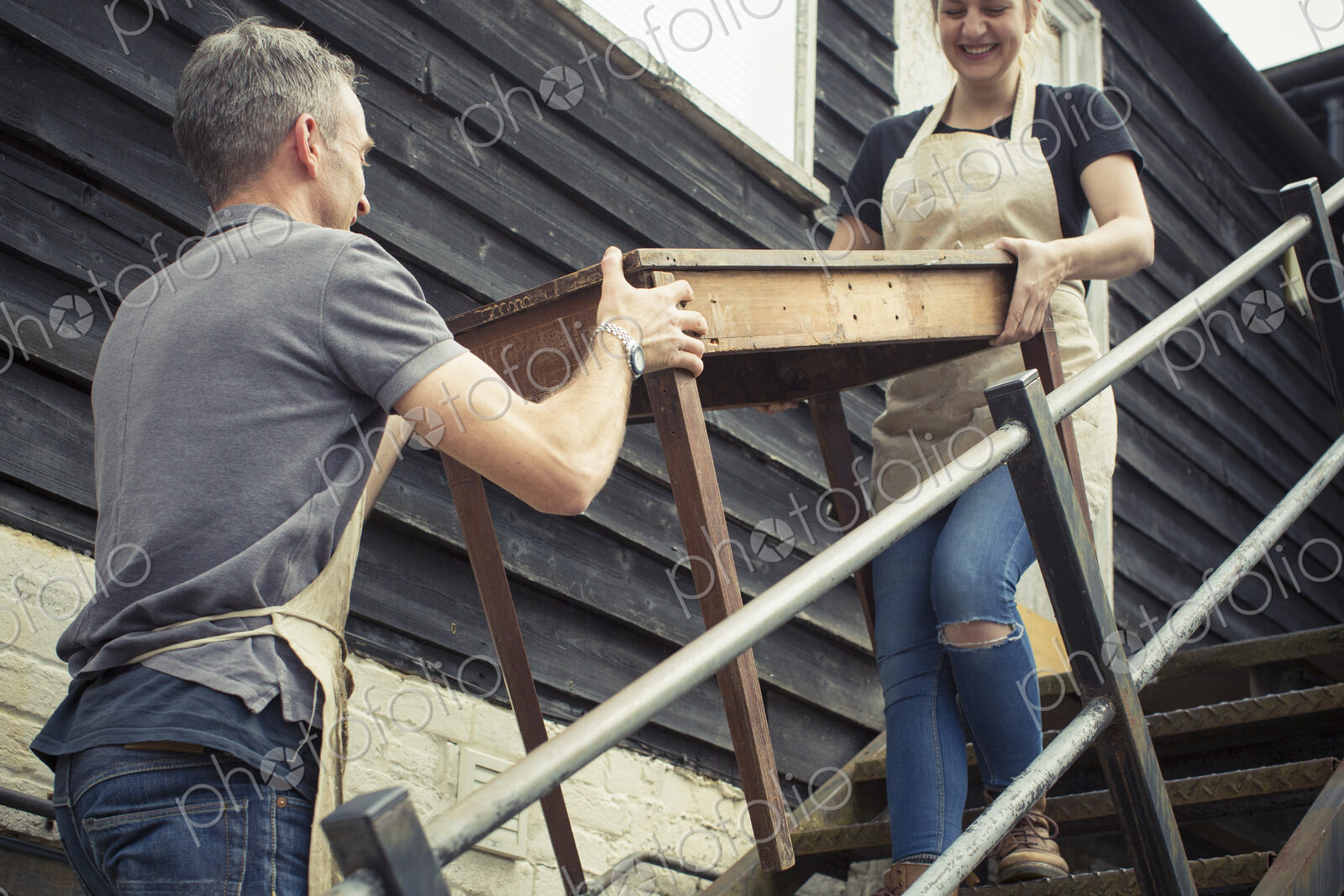 Two people, a man and a young woman carrying an antique wooden table up steps.