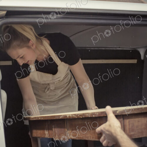 Two people, a man and a young woman lifting an antique wooden table into the back of a… Two people, a man and a young woman lifting an antique wooden table into the back of a…