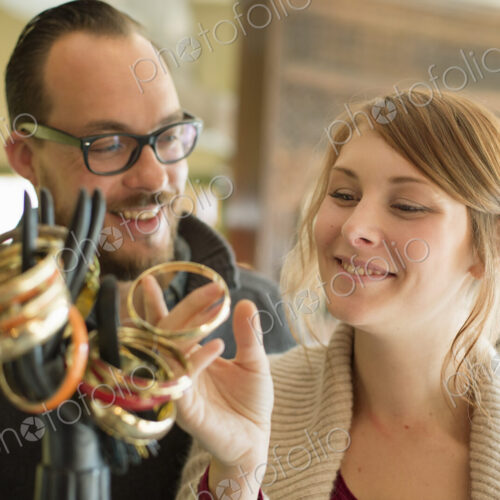Two people, a man and woman looking at the objects displayed on a mannequin hand,… Two people, a man and woman looking at the objects displayed on a mannequin hand,…