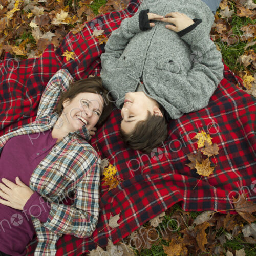 Two people, a woman and a child, lying on a red tartan picnic blanket, looking upwards. Two people, a woman and a child, lying on a red tartan picnic blanket, looking upwards.