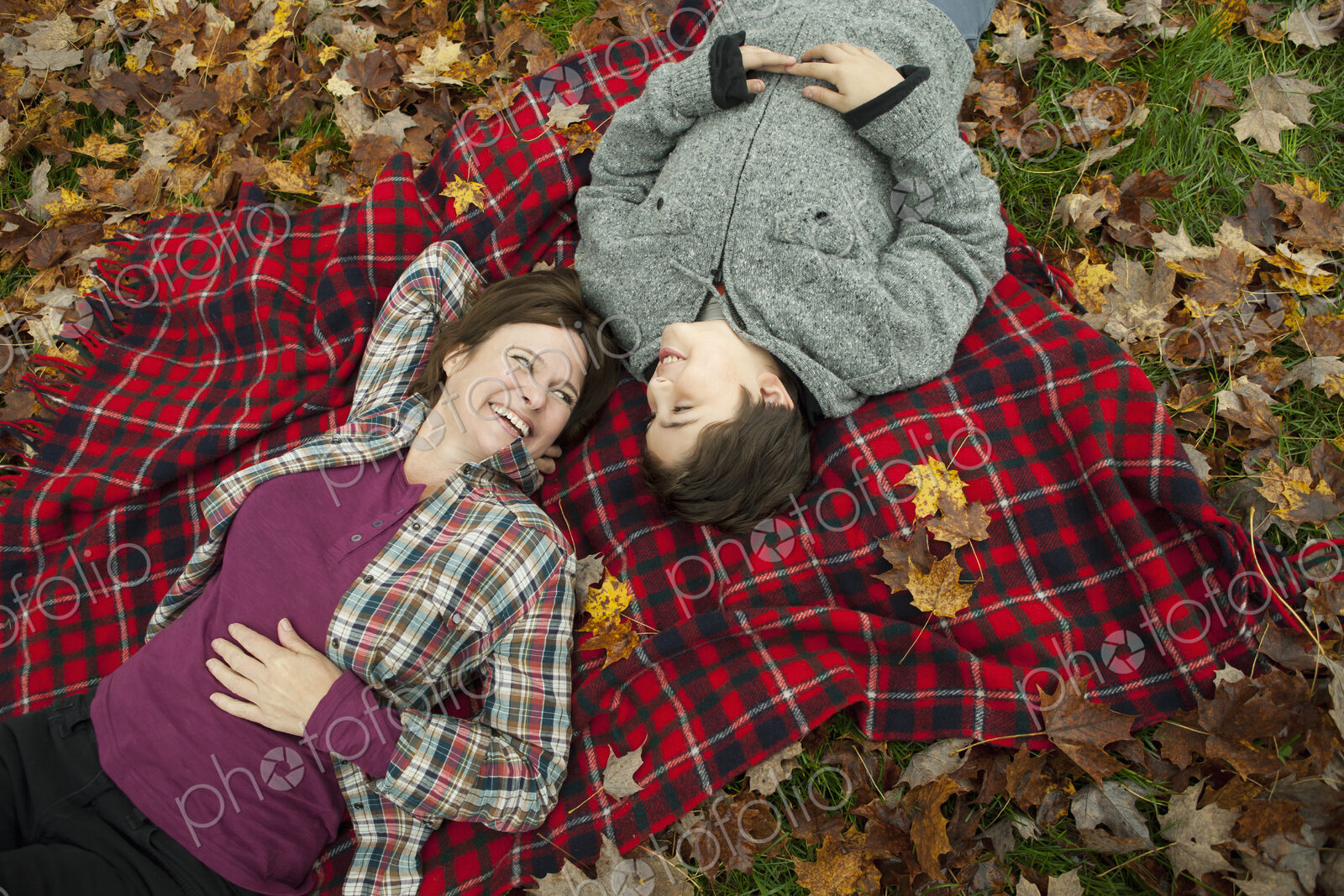 Two people, a woman and a child, lying on a red tartan picnic blanket, looking upwards.