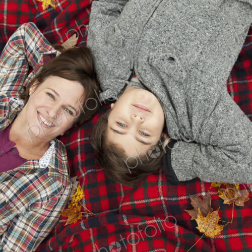 Two people, a woman and a child, lying on a red tartan picnic blanket, looking upwards. Two people, a woman and a child, lying on a red tartan picnic blanket, looking upwards.