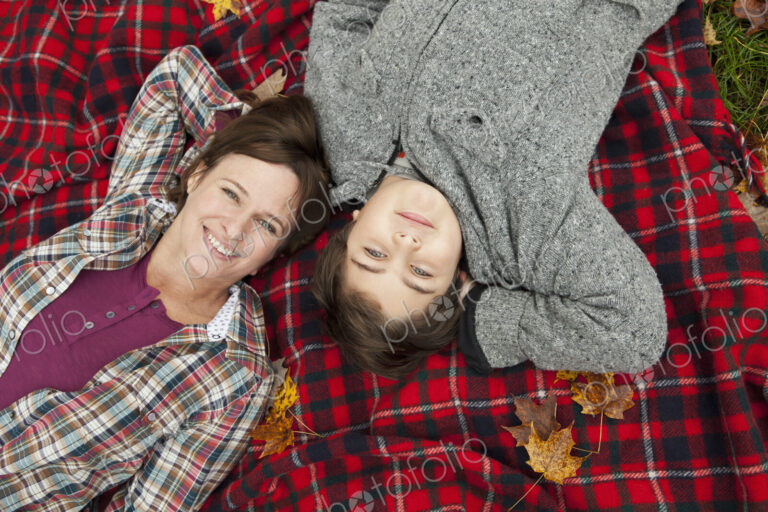Two people, a woman and a child, lying on a red tartan picnic blanket, looking upwards.