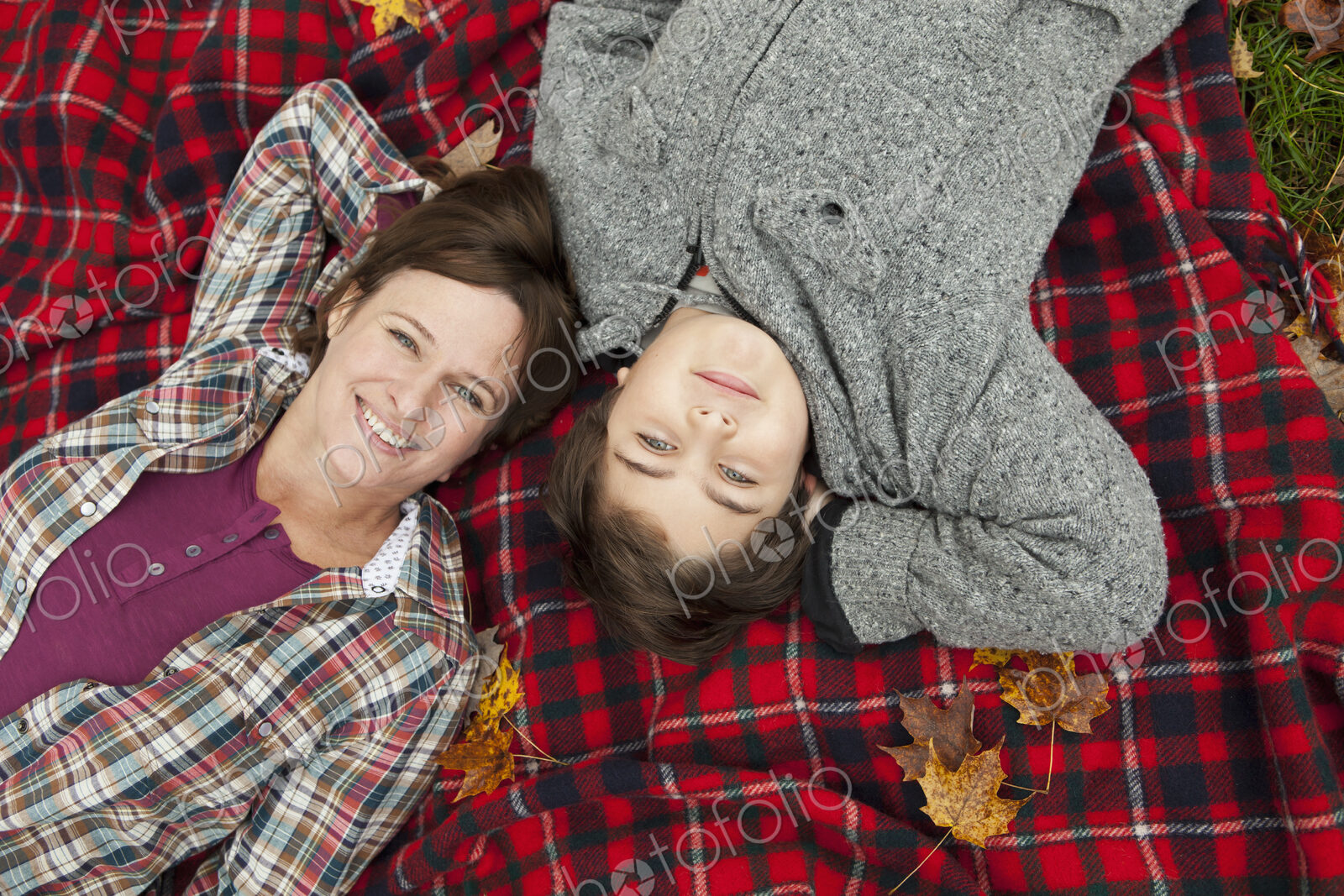 Two people, a woman and a child, lying on a red tartan picnic blanket, looking upwards.