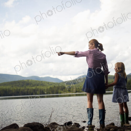 Two people, a woman and a child standing side by side and looking over water.