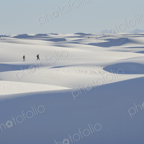 Two people at a distance walking across white sand dunes. Two people at a distance walking across white sand dunes.