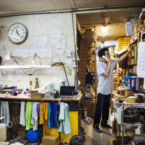 Two people at work in a glass maker's workshop and office, one on the phone.