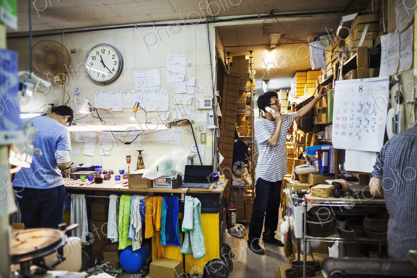 Two people at work in a glass maker’s workshop and office, one on the phone.