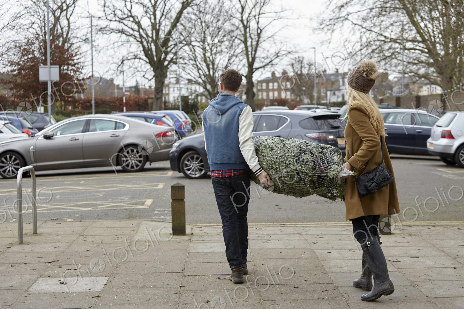 Two people carrying a netted Christmas tree to the car park.
