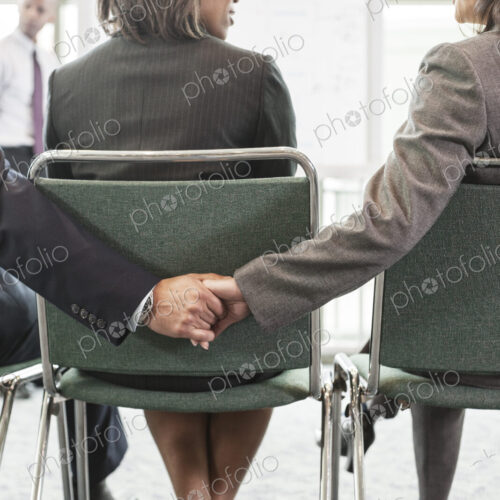 Two people in a businessmeeting holding hands between a third. Two people in a businessmeeting holding hands between a third.
