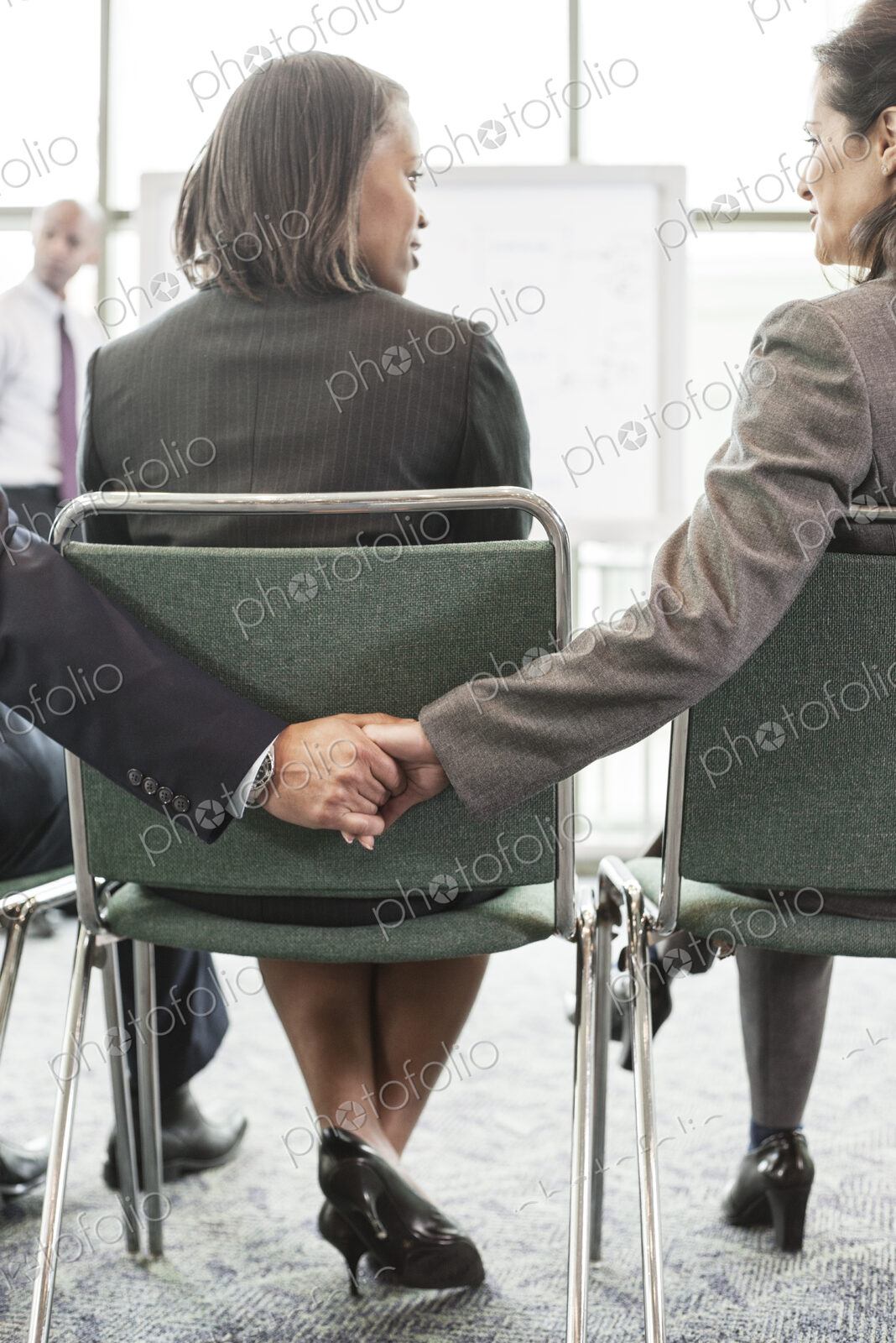 Two people in a businessmeeting holding hands between a third.