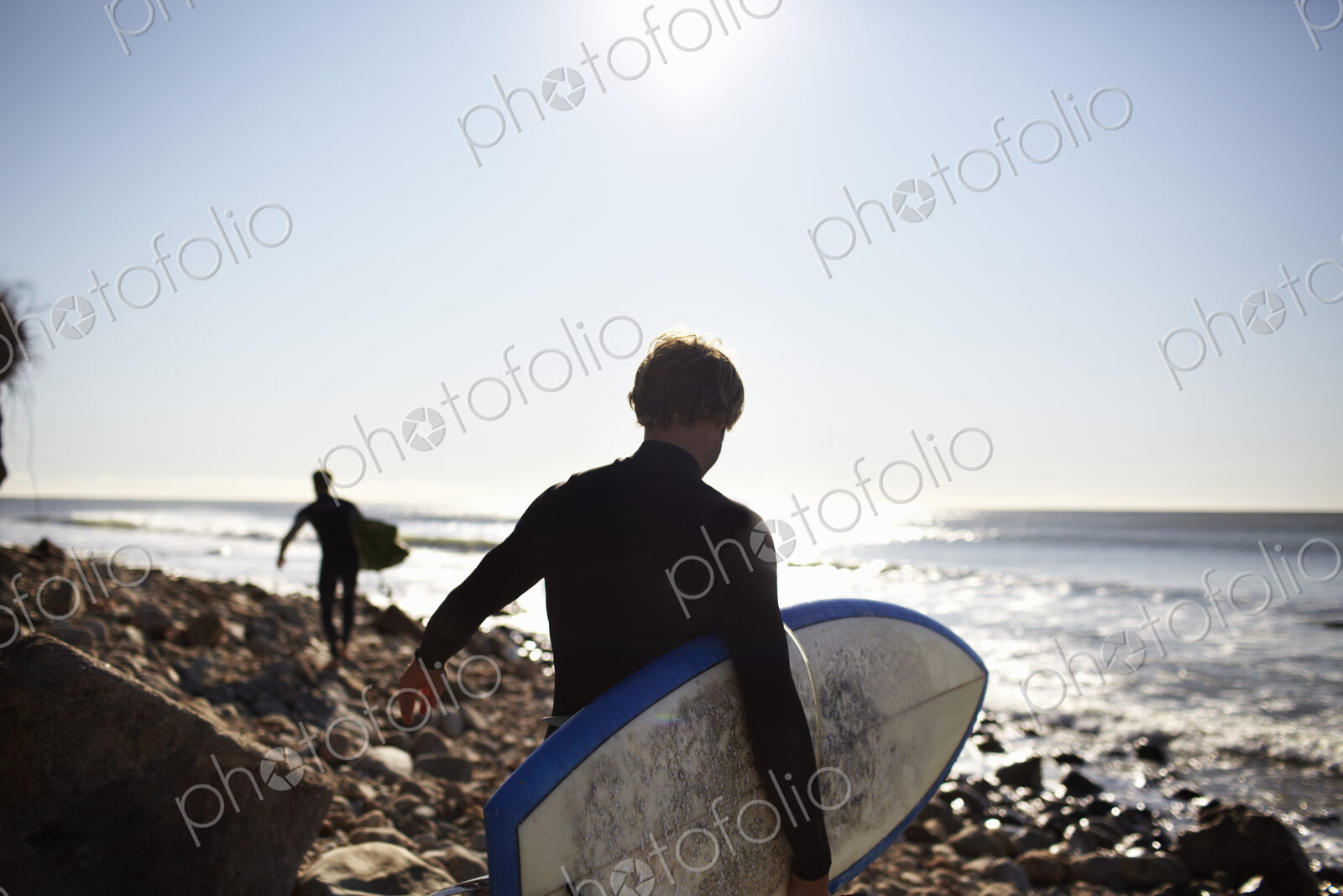 Two people in wetsuits on a beach, carrying their surfboards.