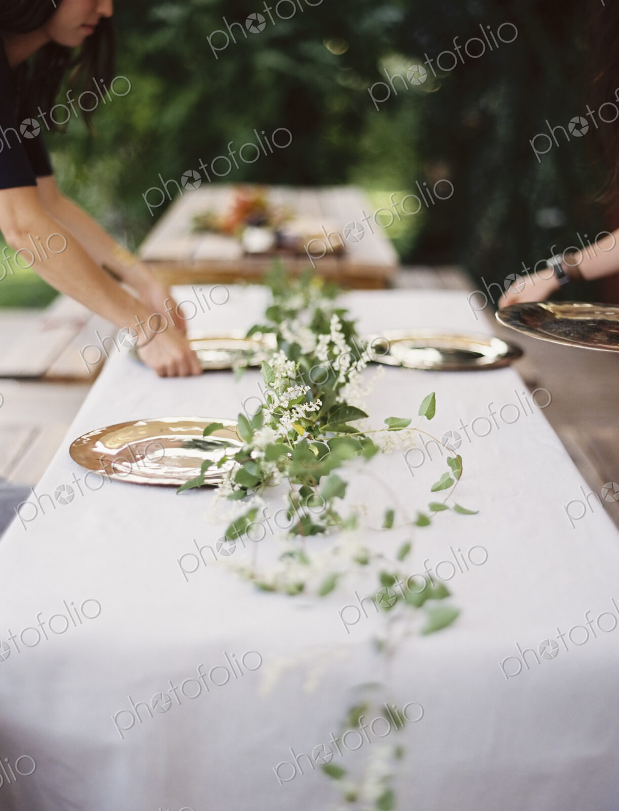 Two people leaning over a table laid outside with a white cloth and a central foliage…
