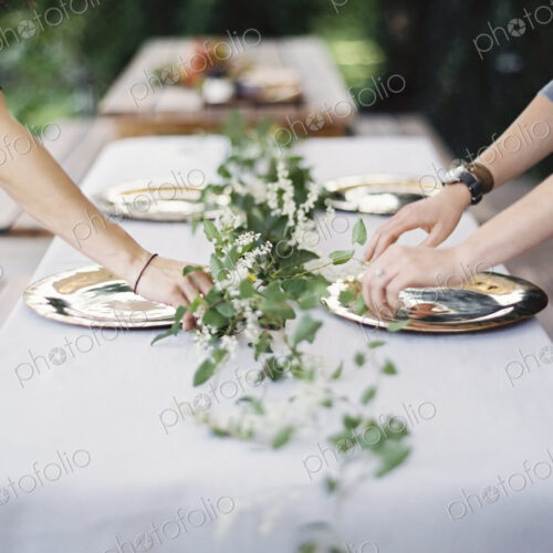 Two people leaning over a table laid outside with a white cloth and a central foliage…