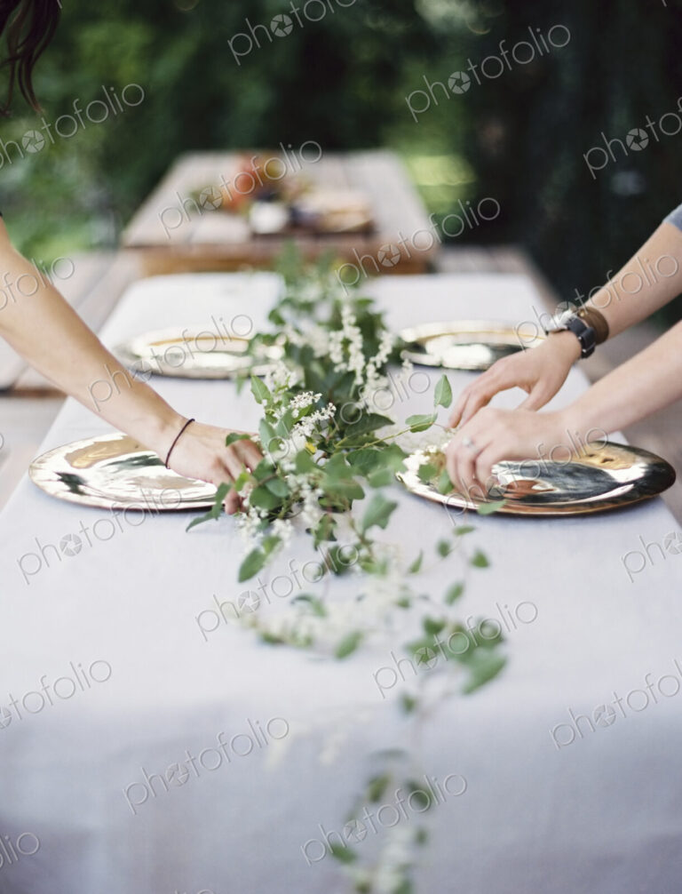 Two people leaning over a table laid outside with a white cloth and a central foliage…